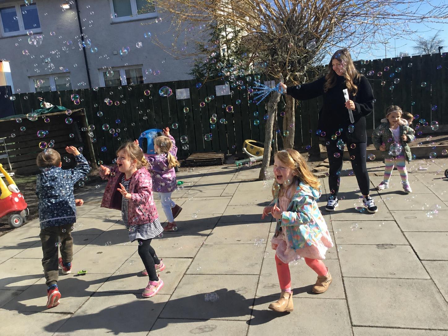 Children chasing bubbles in the garden with a practitioner