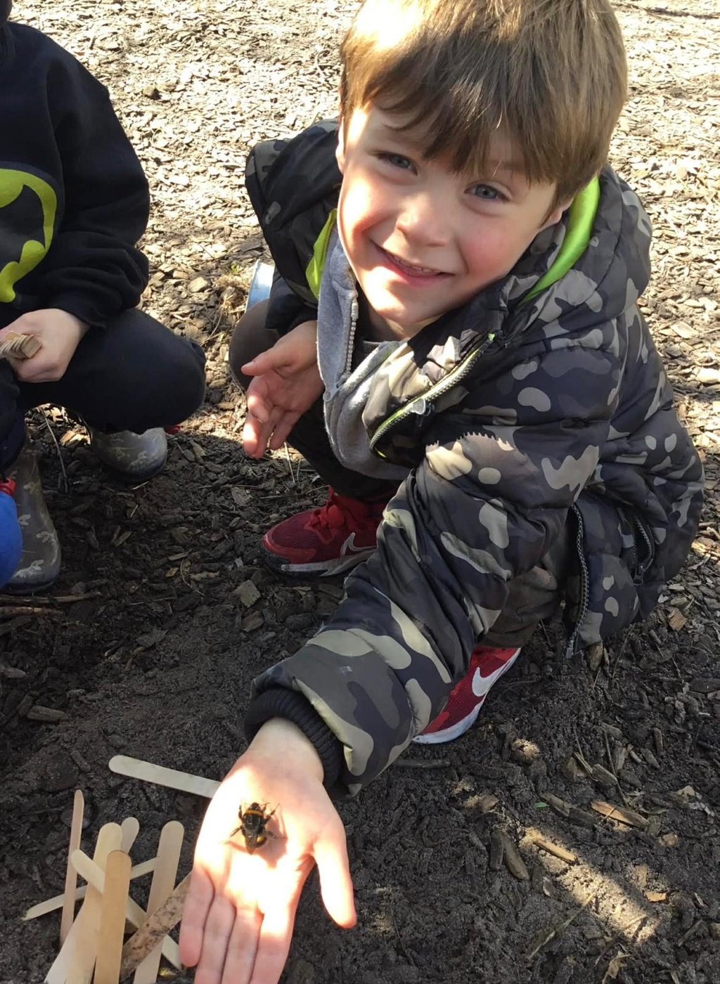 A happy child at Doodlebugs holding a bee during an outdoor forest session